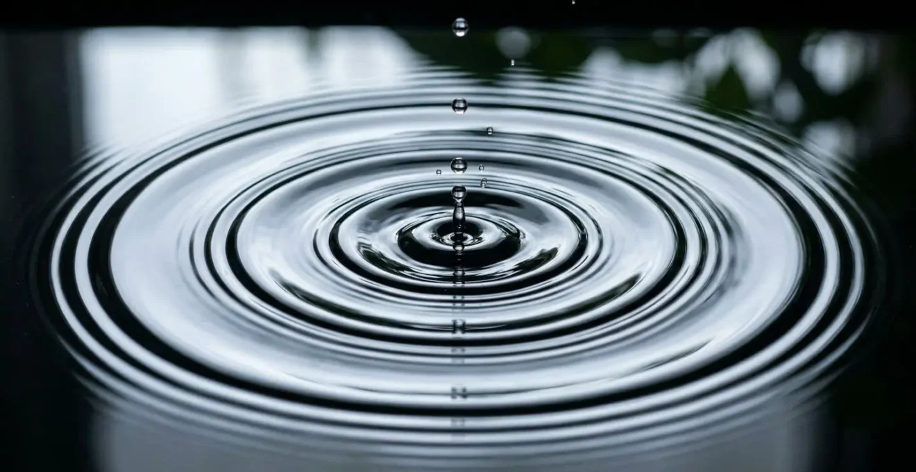 Photographie macro de gouttes d'eau tombant régulièrement sur une surface créant des ondulations concentriques
